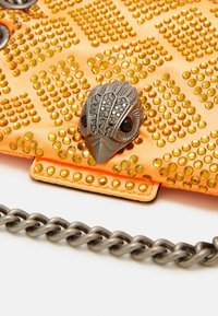 Oranžové saténové psaníčko zdobené žlutými nýty, se stříbrnou sponou ve tvaru ptáka s černými akcenty a stříbrným řetízkovým popruhem.