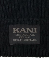 Svart strikket lue med ribbet tekstur. Har en rektangulær svart stofflapp med "KANI"-logoen og varemerkeopplysninger i grått.