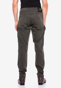 Khaki broek met een relaxte pasvorm, vijf zakken en verstevigde stiksels. Beschikt over een zwart merkembleem op de tailleband. Glad textuur van de stof.