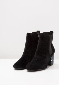 Bottines noires avec une finition en suède texturé, des panneaux latéraux élastiques et un talon bloc pailleté. Présente un design à bout pointu.
