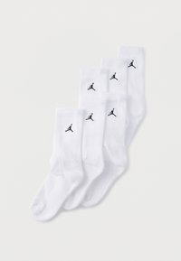 Cinco pares de calcetines blancos hasta el tobillo con un logo Jumpman negro en la parte superior acanalada, dispuestos superpuestos sobre un fondo blanco.