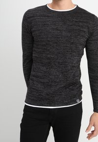 Pull à manches longues noir et gris marbré avec un col rond et une bordure blanche au niveau du col, présentant un motif texturé subtil et un design ajusté.
