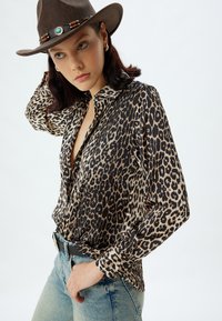 Chemise en tissu soyeux à imprimé léopard, dotée d'un col et d'une fermeture à boutons. Associée à un denim bleu clair et un chapeau de style western brun.