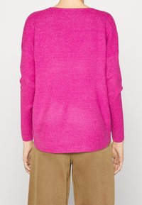 Jersey de punto rosa con un corte relajado, cuello redondo y mangas largas; presenta una textura suave y dobladillo acanalado. Combinado con pantalones beige.