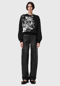 Felpa nera con design a stampa leopardata, maniche a palloncino, polsini a coste, abbinata a pantaloni larghi in pelle nera e scarpe flat.