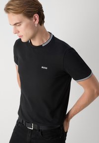 Sort kortærmet t-shirt med rund hals, der har hvide striber, lille "BOSS" logo på brystet og en tætsiddende silhuet.