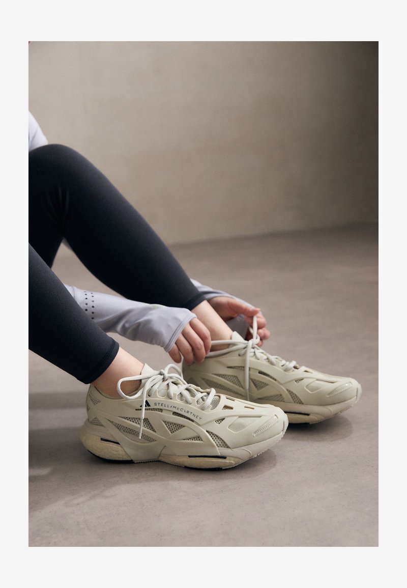 Adidași verzi deschis cu un design din plasă, vârf rotund și șireturi albe. Talpa este ușor ridicată, oferind amortizare.