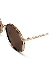 Pyöreät aurinkolasit, joissa on kilpikonnankuoriväriinen kehys, kultasävyiset metalliset varret ja tummanruskeat linssit. Varressa on brändin nimi "Kapten & Son".