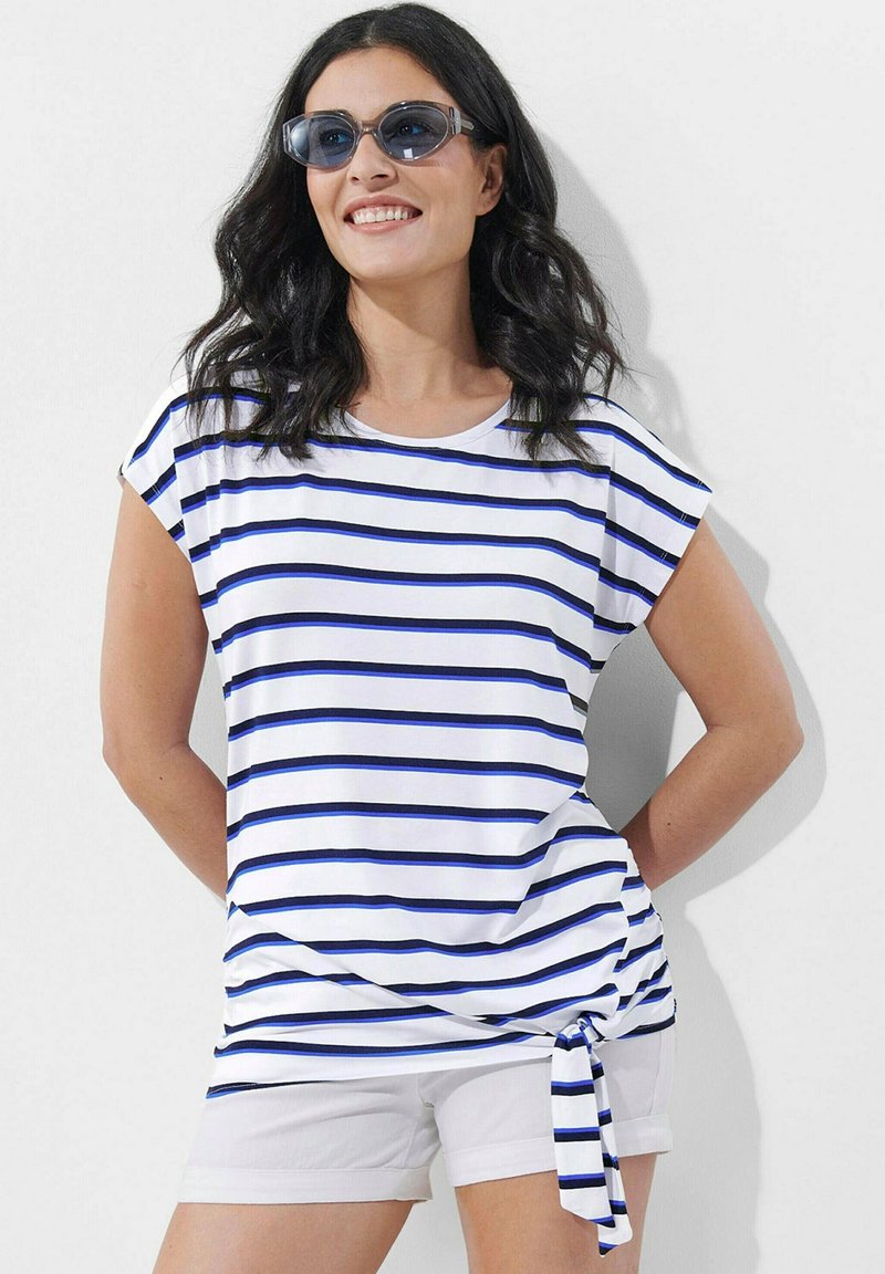 Weißes T-Shirt mit blauen Streifen, kurzen Ärmeln und einem geknoteten Seitendetail, kombiniert mit weißen Shorts. Glattes Material mit lässigem Schnitt.