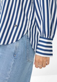 Gestreepte blouse met marineblauwe en witte verticale lijnen, knoopmanchetten en een afgeronde zoom, gecombineerd met lichtblauwe denim jeans.