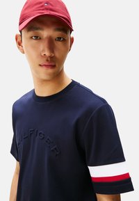 Camiseta de manga corta de la Marina con logo en relieve, con acentos en blanco y rojo en los puños. Material de algodón suave con un cuello redondo.