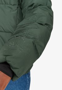 Giacca a vento verde con design trapuntato, caratterizzata da una texture resistente all'acqua. Piccole gocce visibili sul tessuto ne aumentano l'idoneità per l'uso all'aperto.