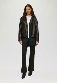 Schwarze Leder-Motorradjacke mit silbernen Beschlägen, über einem dunklen Pullover getragen, kombiniert mit schwarzen Schlaghosen und spitzen Ankle-Boots.