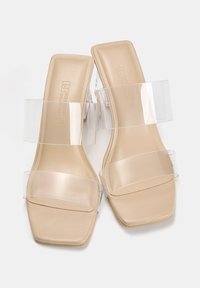 Beige Sandalen mit Blockabsatz und transparenten Riemen, quadratische Zehen und einer glatten Lederoberfläche, gestaltet im minimalistischen Stil.