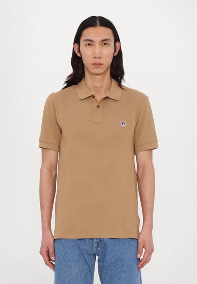 Polo shirt à manches courtes en coton tan, avec un col et un petit logo de chien multicolore brodé sur la poitrine gauche.