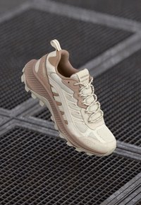 Chaussure de randonnée beige et tan avec une tige en maille respirante, une languette rembourrée, une semelle texturée et des accents de marque subtils. Conception légère.