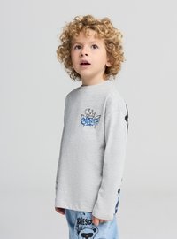 Szary długi rękaw t-shirt z niebieskim wzorem na piersi. Dziecko ma na sobie niebieskie dżinsy z grafiką pandy.