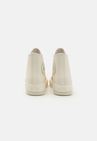 Magas szárú sneakers off-white bőrből, sima textúrával, domború csillaglogóval, gumitalppal és varrott részletekkel.
