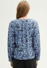 Blue patterned blouse featuring varying shades of blue, black, and white dots, long sleeves, gathered neckline, and buttoned cuffs.