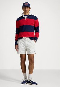 Μπλούζα πόλο με μακριά μανίκια σε κόκκινες και ναυτικές ρίγες, λευκά σορτς, μπλε αθλητικά παπούτσια, λευκές κάλτσες και μπλε καπέλο. Διαθέτει κλασικό σχεδιασμό με γιακά.