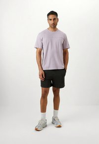 Ljuslila t-shirt med korta ärmar och rund halsringning, kombinerad med svarta shorts. Silvriga träningsskor med orange detaljer och vita strumpor.