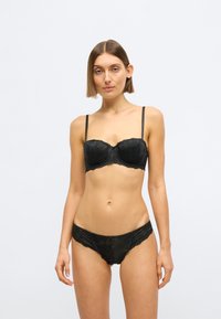 Črni čipkasti komplet spodnjega perila z oblazinjenim balkončnim modrcem z dekorativnimi cvetličnimi vzorci in ujemajočimi se nizkimi hlačkami z robom iz čipke.