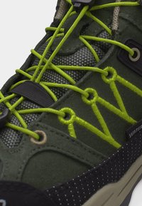 Κλείσιμο σε πράσινο και μαύρο αδιάβροχο αθλητικό παπούτσι με φωτεινά κίτρινα ελαστικά κορδόνια και υφασμάτινη γλώσσα με υφή.