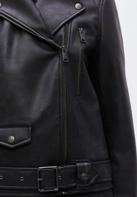 Schwarze Leder-Motorradjacke mit strukturiertem Finish, asymmetrischen Reißverschlüssen, Druckknopf-Akzenten und tailliertem Gürtel.