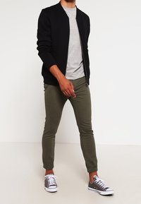 Černá bomber bunda, světle šedé tričko s kulatým výstřihem, olivově zelené zúžené kalhoty a šedé tenisky s bílými tkaničkami. Neformální outfit.