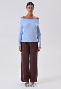 Maglioneazzurro chiaro con spalle scoperte e texture a coste, abbinato a pantaloni larghi marroni; scarpe argentate a punta aggiungono contrasto.