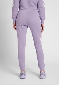 Hellblaue Jogginghose mit schmal zulaufendem Design, elastischem Bund und weißen Chevron-Details an den Seiten. Kombiniert mit passenden Sneakers.
