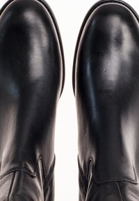 Black leather ankle boots with a smooth texture, rounded toes, and stitched seam detailing, viewed from a top-down perspective.