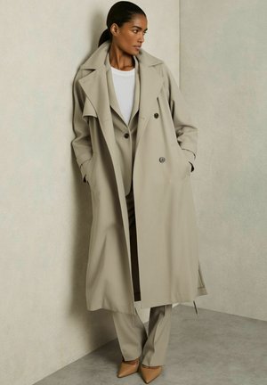 Bež trench coat, mille avatud disainiga, suurte kraedega ja küljetaskutega, kantud ühilduva ülikonna ja valge särgi üle. Üksik terav tan-kolm saadud kõrgendavate kingadega.