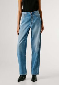 Vaqueros de tiro alto azul claro con un diseño de pierna ancha, textura desteñida y bolsillos. Combinados con botines negros de tacón.