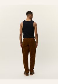 Zwarte mouwloze top gecombineerd met bruine corduroy broek. De broek heeft twee achterzakken en heeft een gestructureerd, ribbelachtig oppervlak.