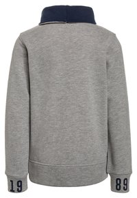 Sudadera gris con cuello azul marino, puños acanalados y números impresos "19" y "89" en las mangas. Textura de tela suave, diseño casual.