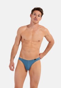 Blå mønstrede herrebikini briefs med et geometrisk design, der har et blødt stof og en tynd elastik, designet til komfort og pasform.