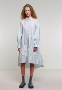 Ljusblå, långärmad skjortklänning med rynkad midja, hög-låg fåll och knappstängning. Glansiga grå ankelstövlar fulländar outfiten.
