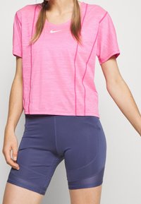 Mujer vistiendo una camiseta de manga corta rosa de Nike y pantalones cortos deportivos ajustados azul marino, mostrada de los hombros hasta la mitad del muslo.
