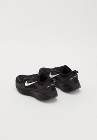 Paire de chaussures de course Nike noires et marron avec logos swoosh blancs, placées côte à côte sur un fond clair uni.