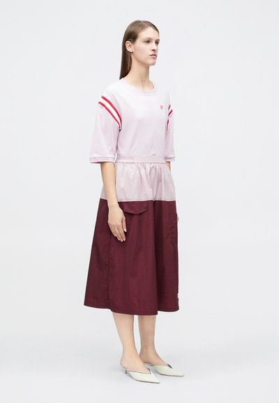 Ανοιχτό ροζ μπλουζάκι με κόκκινες ρίγες, συνδυασμένο με μπορντό φούστα που διαθέτει μπροστινή τσέπη και σφιχτή μέση για εφέ με στρώσεις.