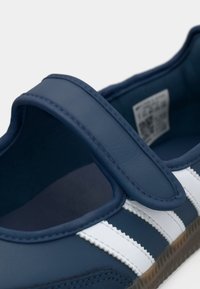 Blå Mary Jane-sneaker med velcrolukning og to hvide striber på siden på en gumssål.