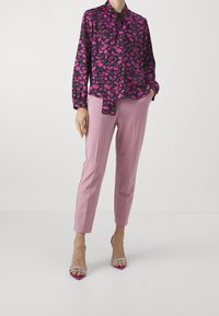 Black shirt with pink lip pattern, tied collar, paired with light pink tapered trousers and clear-heeled sandals.