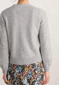 Jasnoszary sweter dziergany o fakturowanej powierzchni, z prążkowanym dołem i balonowymi rękawami, zestawiony z wielokolorową spódnicą w kwiaty.