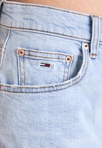 Světle modré džíny z denimu mají malou zadní kapsu s vícerozměrným logem a měděné kovové detaily na pasu a kapse.