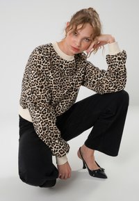 Sweat-shirt à imprimé léopard avec des poignets et un col crème, associé à un pantalon large noir et des talons aiguilles noirs.
