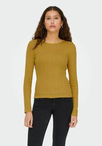 Sennepsgul ribbet langærmet top med rund halsudskæring, der har subtile lodrette mønstre og en tætsiddende silhuet. Kombineret med sorte jeans.
