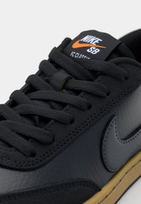 Sapatilhas Nike SB de couro preto com atacadores planos, apresentando uma língua acolchoada, o famoso swoosh e uma sola de borracha de cor caramelo com detalhes texturizados.