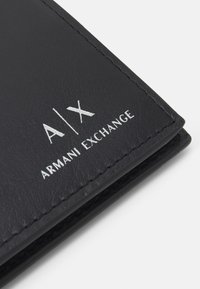 Portafoglio in pelle nera con logo in rilievo "A|X" e "ARMANI EXCHANGE" in argento, con cuciture visibili e texture liscia.