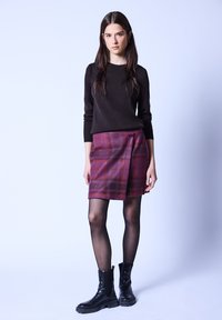 Czarny sweter z długim rękawem w połączeniu z bordową kraciastą spódnicą z wąskim paskiem z guzikiem. Modelka nosi czarne sznurowane botki do kostek.